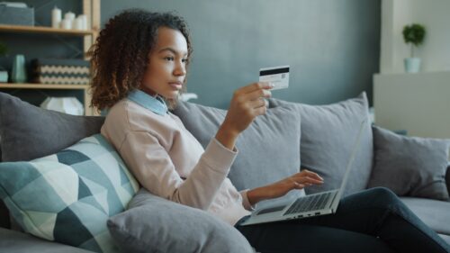 Woman using laptop and credit card on sofa