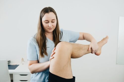 A physiotherapist assisting a patient's leg therapy session indoors, focusing on rehabilitation.