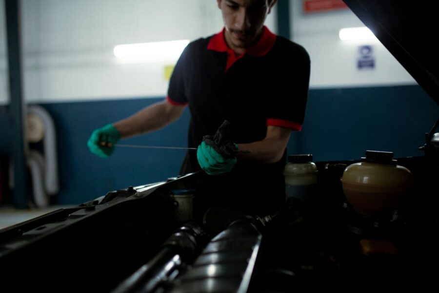 Mechanic examining a car engine's oil level using a dipstick in a garage setting.